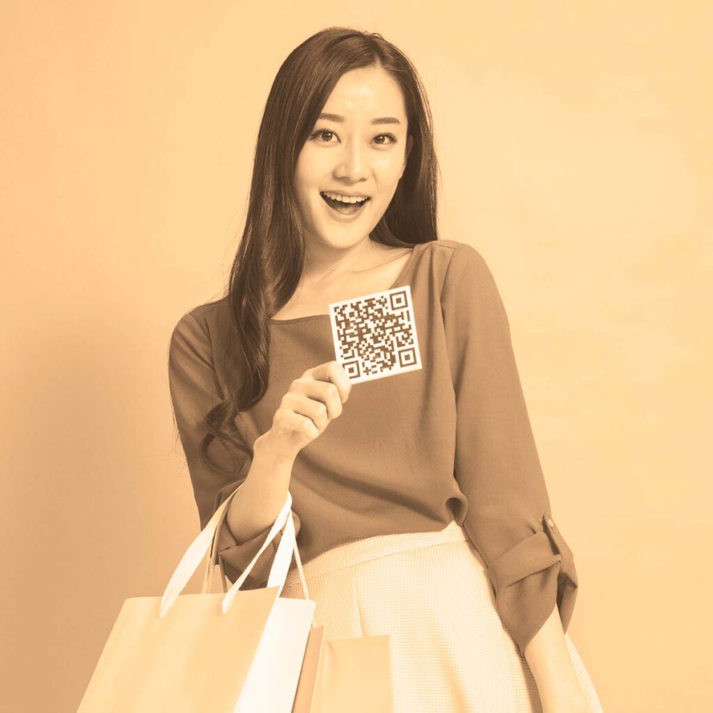 A happy retail customer holding shopping bags and a printed square QR code flyer, created using a free custom QR code generator to boost offline sales.