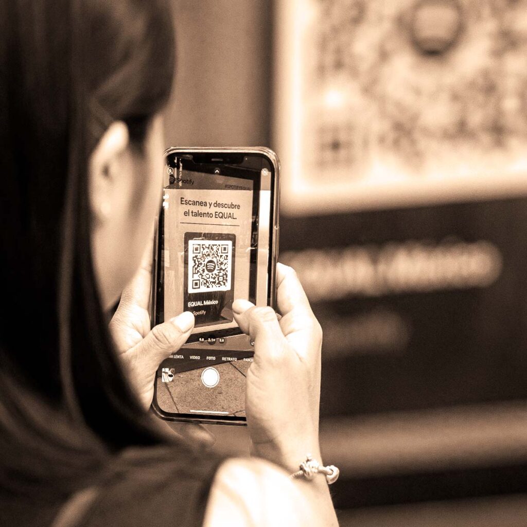A person using a smartphone camera app to scan a large dynamic QR code with an embedded logo displayed on a public advertising billboard.